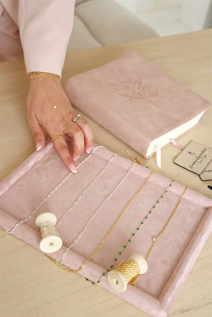 Hand arranging delicate necklaces on pink velvet tray.