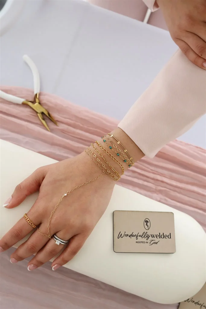 Gold bracelets on wrist with jewelry tool nearby.