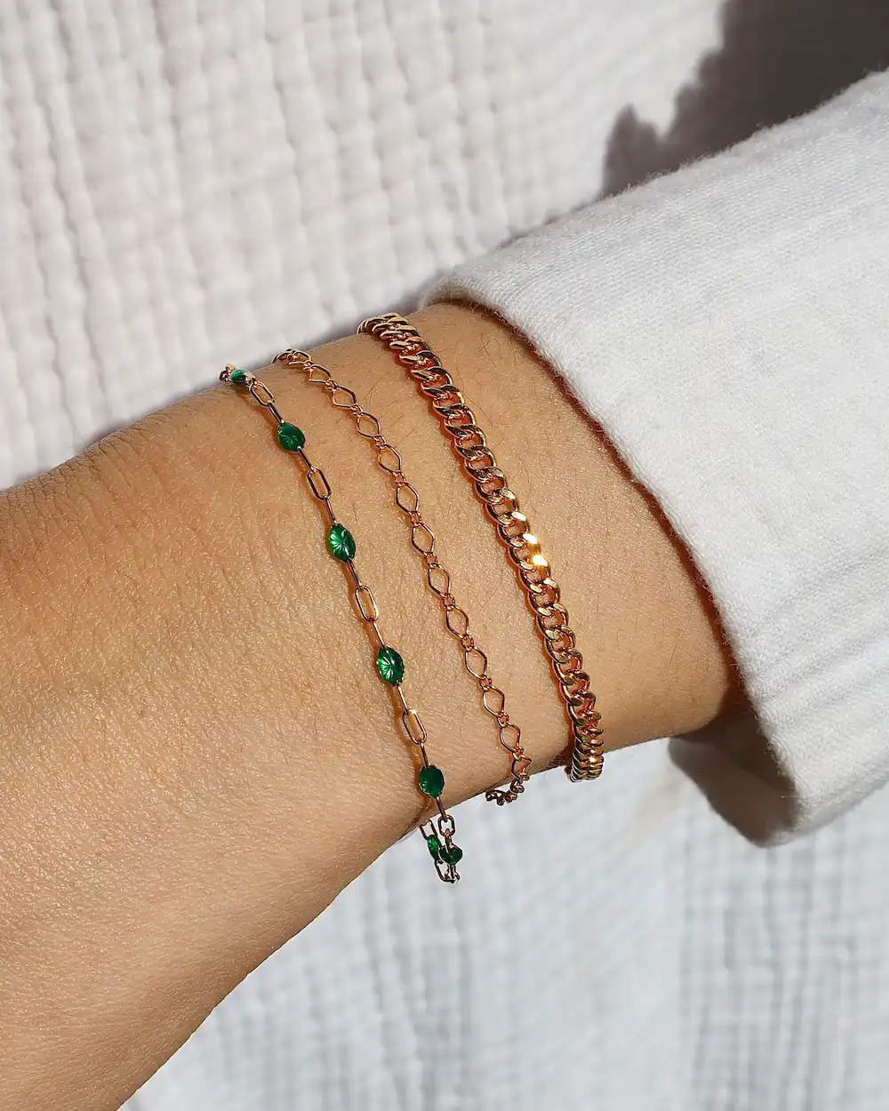 Three gold bracelets on wrist with green stones.