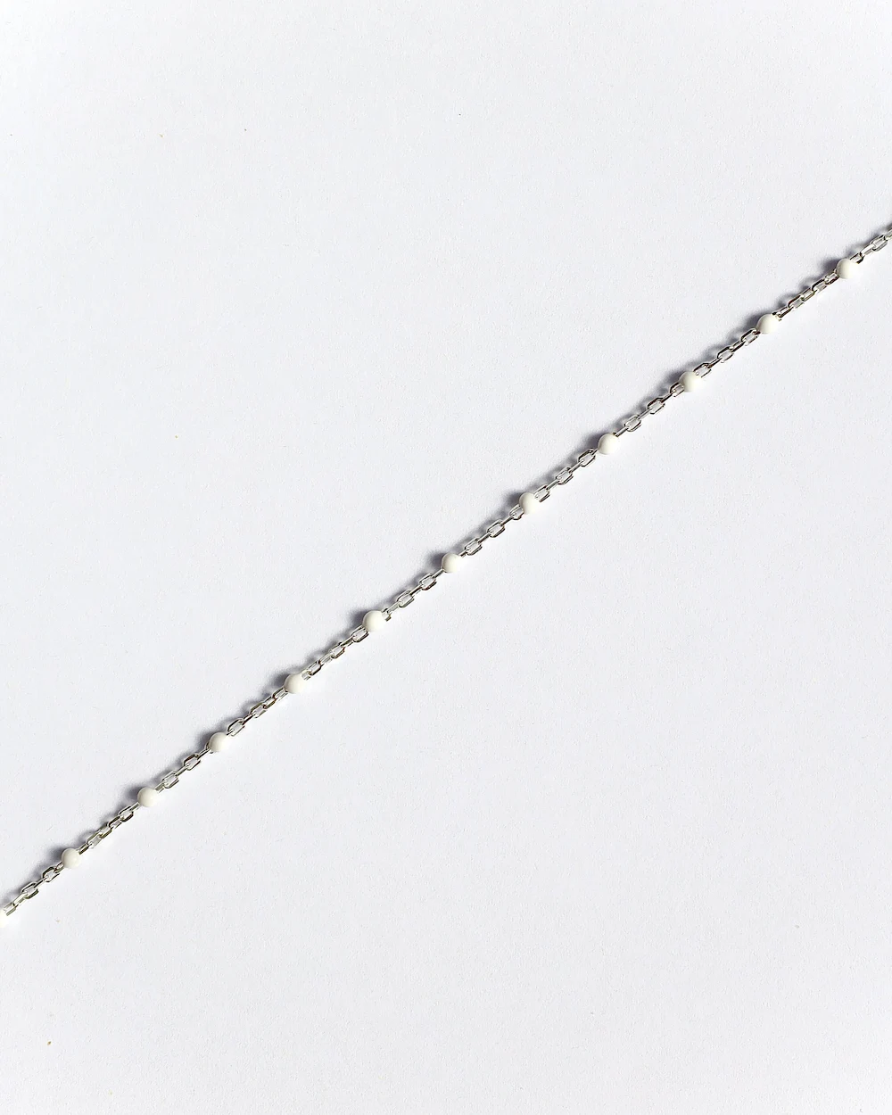 Thin silver chain with small beads on plain background.